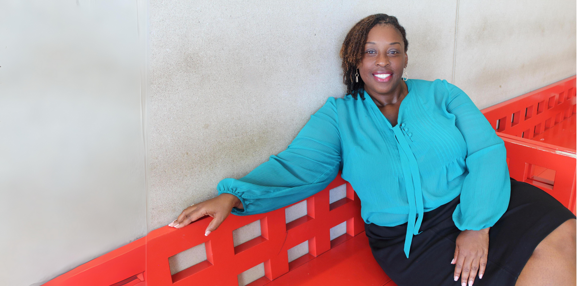Professor Allen in a blue shirt and black skirt sitting on a red bench.